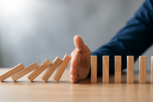 Hand stopping a row of falling wooden dominoes, representing business continuity management and operational resilience.